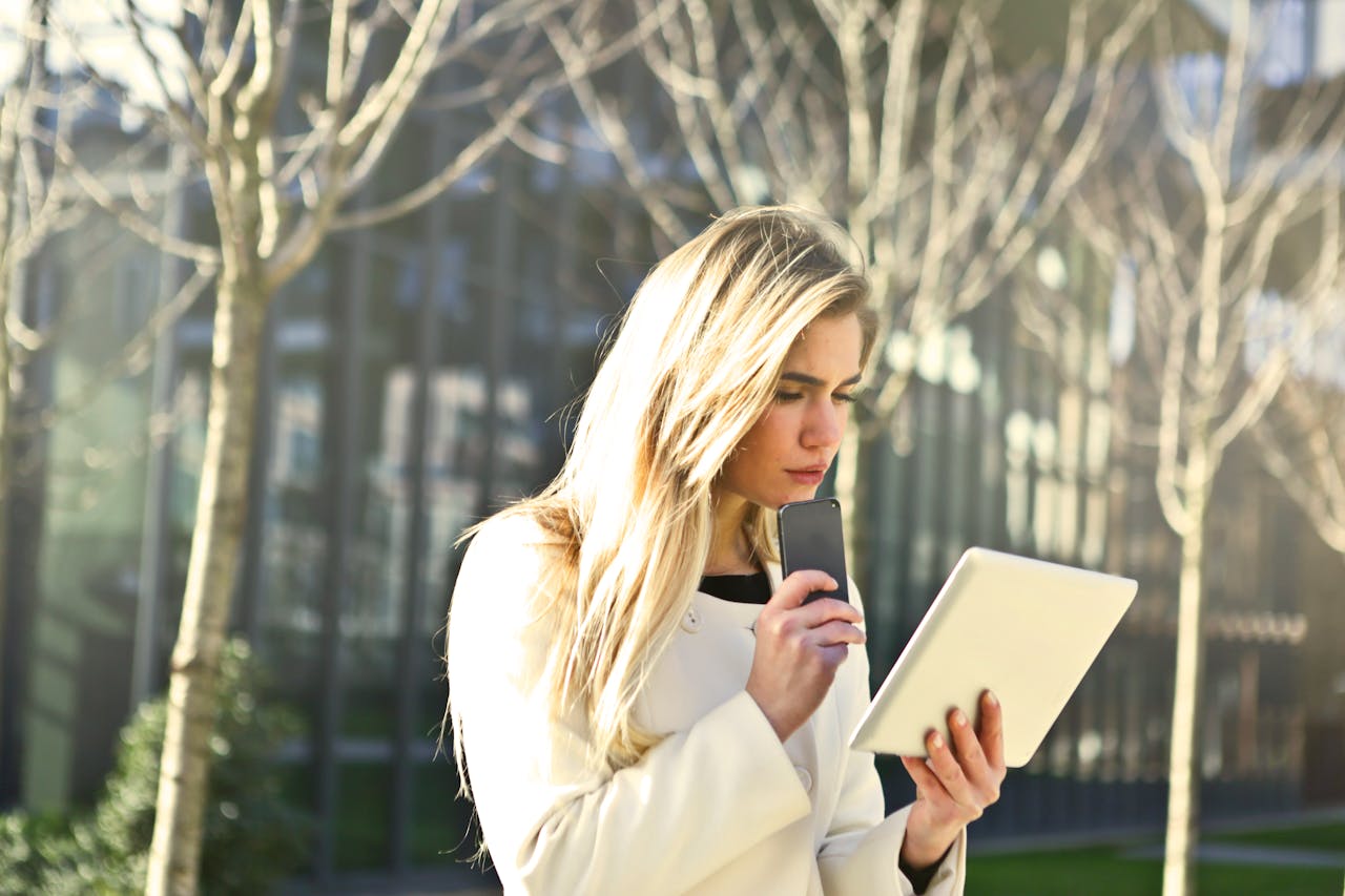 A young woman using her tablet and smartphone outdoors in a city park.