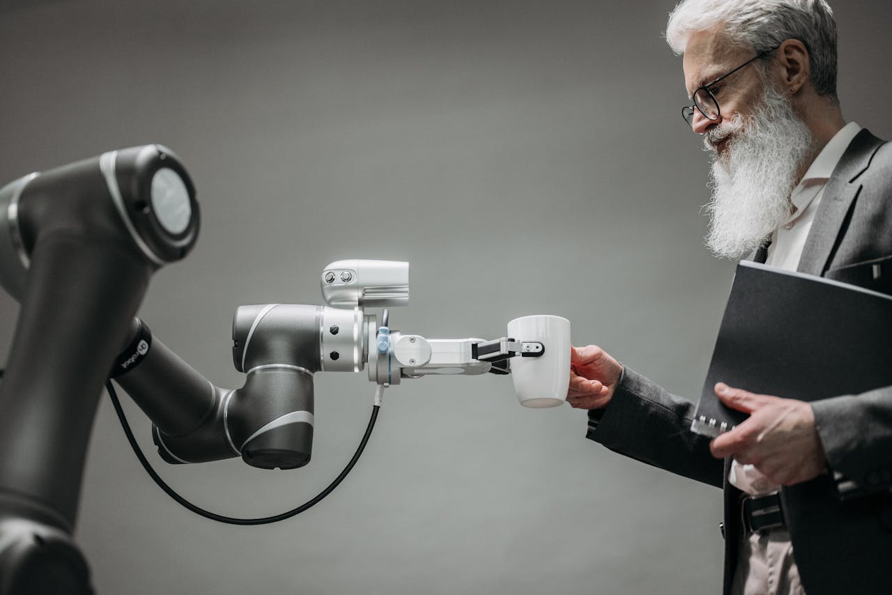 Home An elderly man receives a cup from a robotic arm in a modern office setting.
