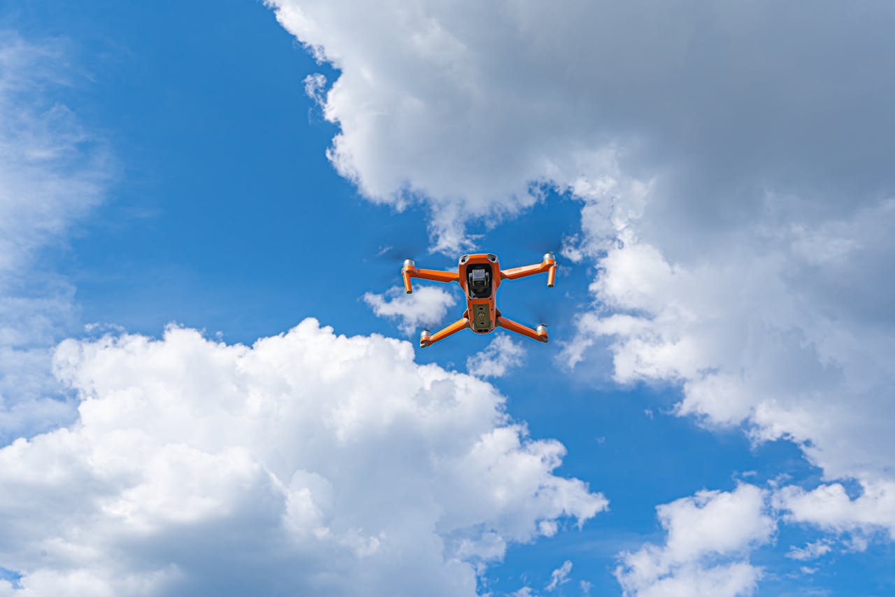 services-04 Orange drone flying against a dramatic cloudy sky, showcasing modern technology and aerial expertise.